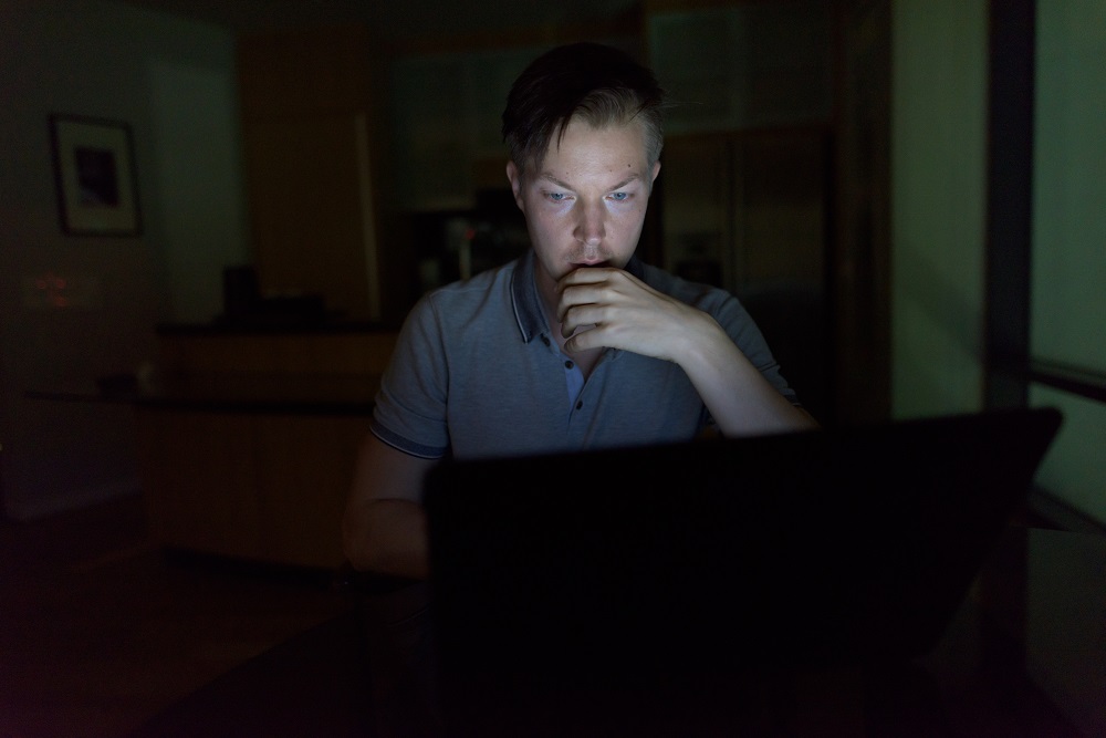 Young handsome man using laptop in the dark living room