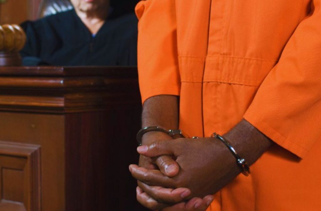 A defendant in a Louisiana courtroom, wearing an orange prison uniform, faces assault charges.