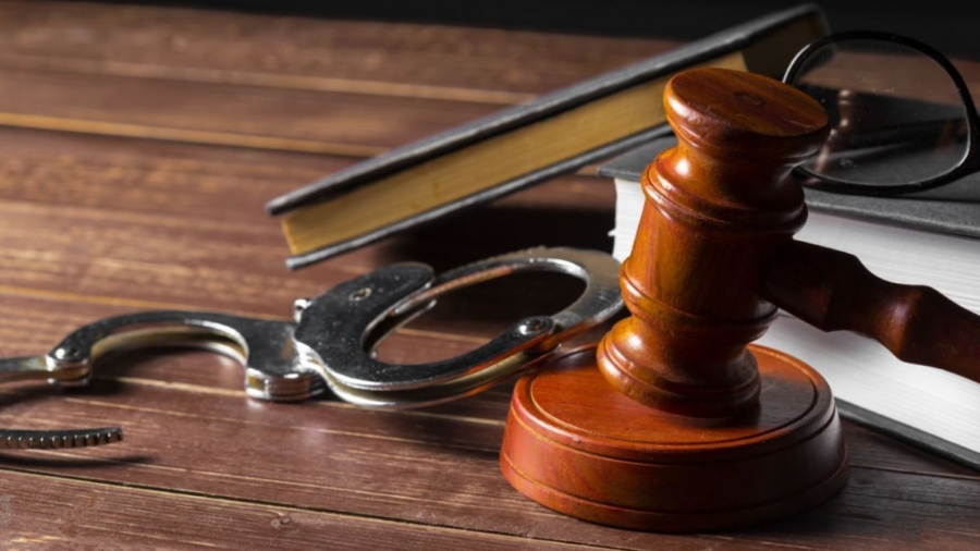 A gavel, handcuffs, and glasses arranged on a wooden table, symbolizing the work of a criminal law attorney.