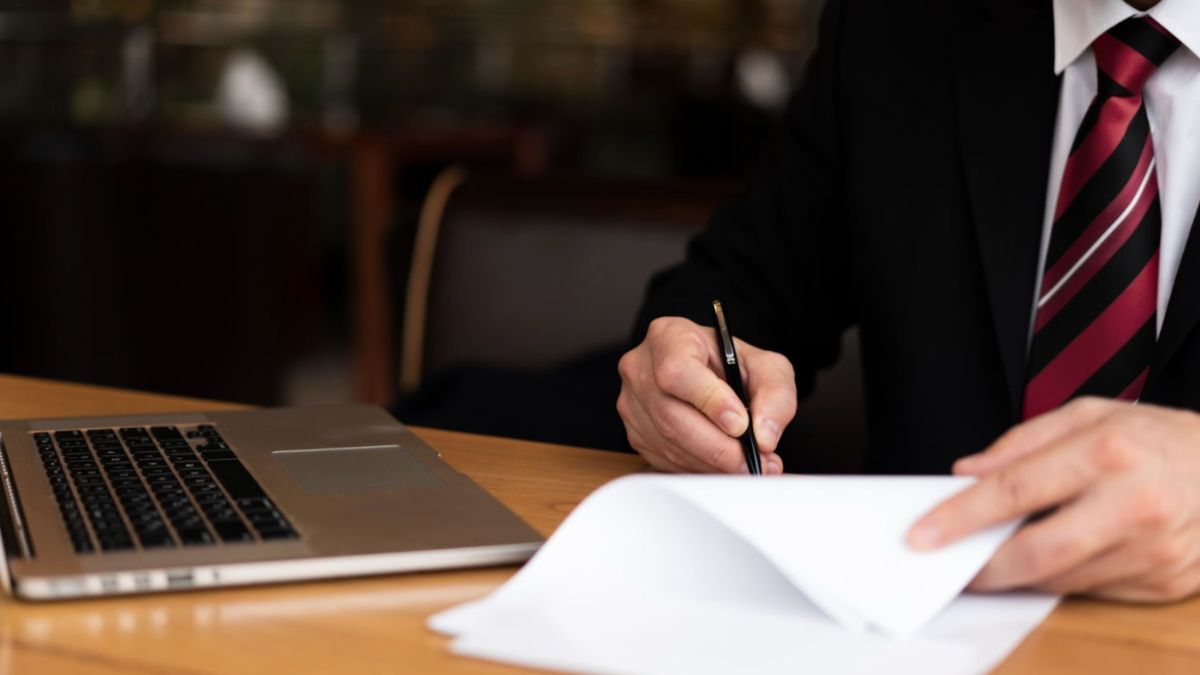 A lawyer in a suit and tie writes on paper, illustrating the critical thinking involved in murder defense strategies.