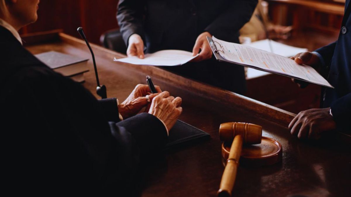 In a courtroom, a judge and two lawyers are seated at a desk, deliberating on legal matters and court procedures.