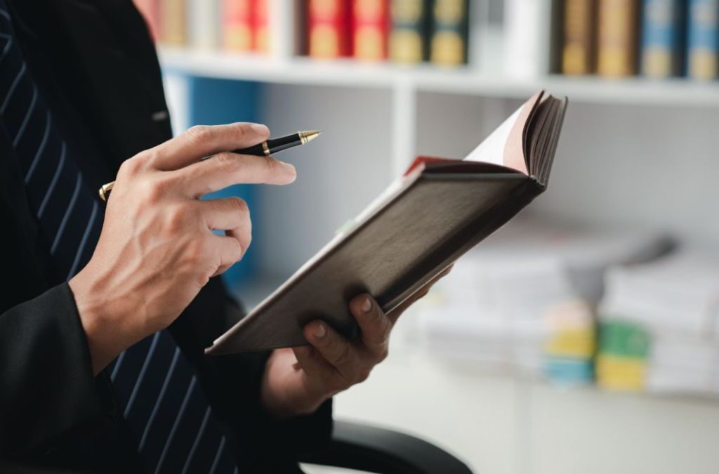 A criminal defense attorney in a suit diligently writes notes in a book.