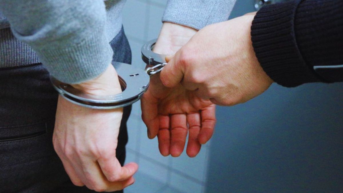 A person is shown from behind with their hands cuffed as an officer secures handcuffs during an arrest.